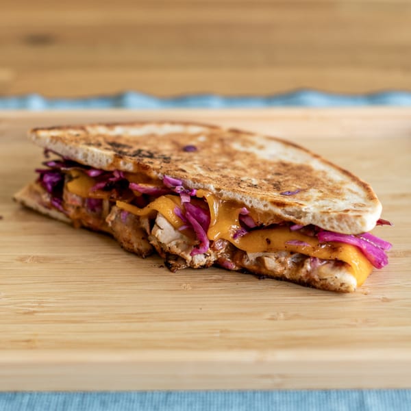 Grilled Indian sandwich with chicken, melted cheese, and purple cabbage on a wooden board.