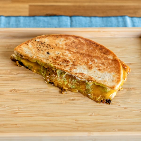 A golden-brown quesadilla with melted cheese and green filling, served on a wooden board.