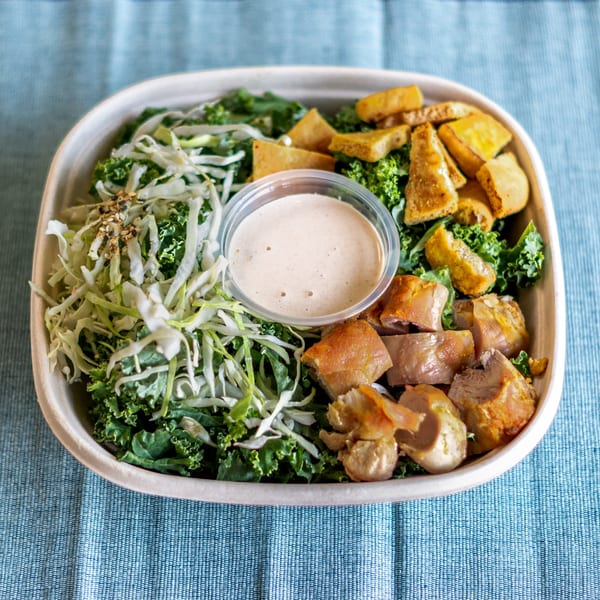 Ruta's Fresh Indian Fare bowl with kale, cabbage, chicken, paneer, and dressing on a blue tablecloth.
