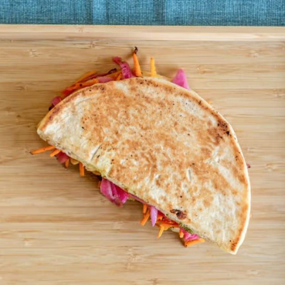 A grilled quesadilla filled with shredded carrots and pickled red onions on a wooden board.