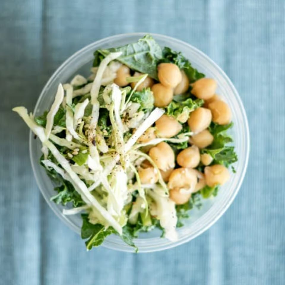 Overhead view of a salad with chickpeas, kale, and shredded cabbage in a clear bowl.