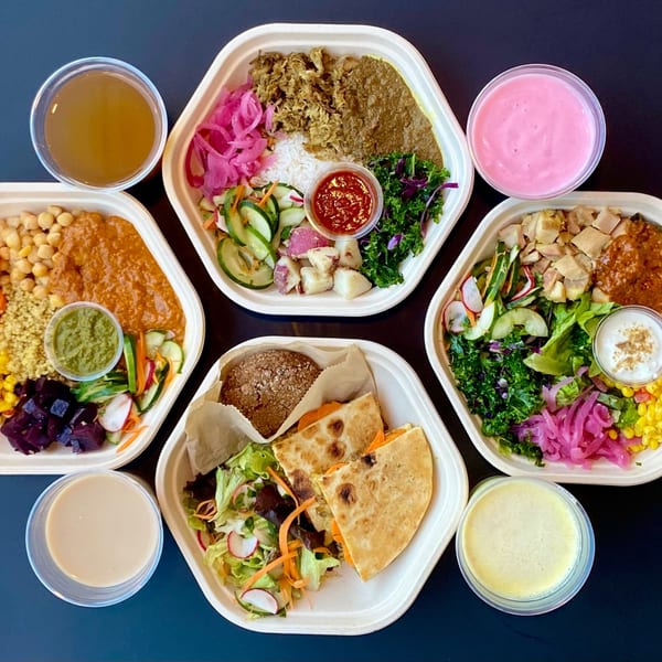 Overhead view of five hexagonal Indian food bowls and four drinks on a dark surface.