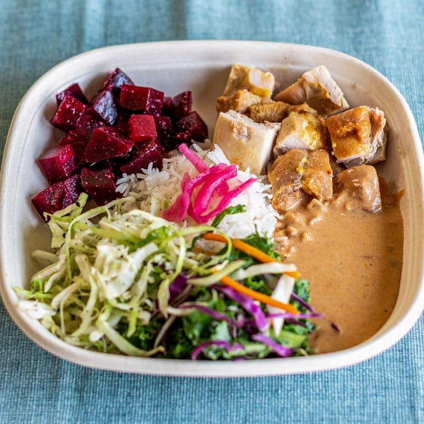 Indian bowl with chicken, rice, beets, pickled onions, and mixed greens on a blue tablecloth.