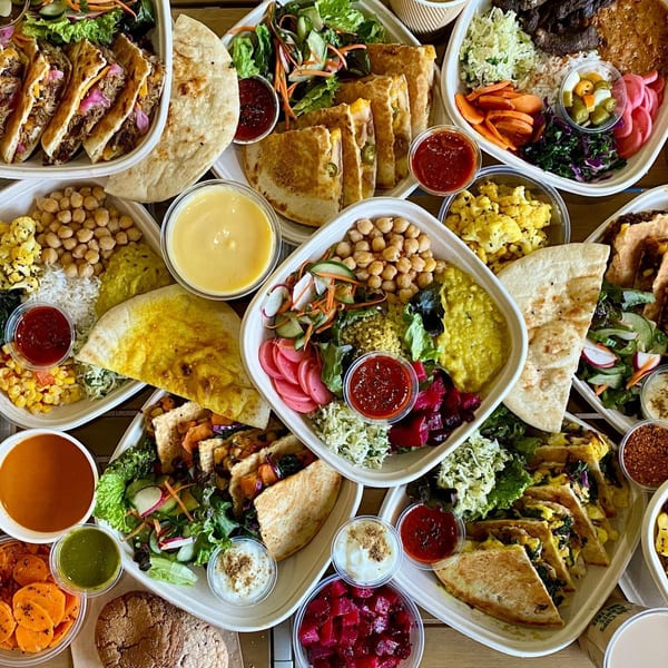 Overhead view of various Indian dishes in takeout containers, including quesadillas, bowls, and sides.