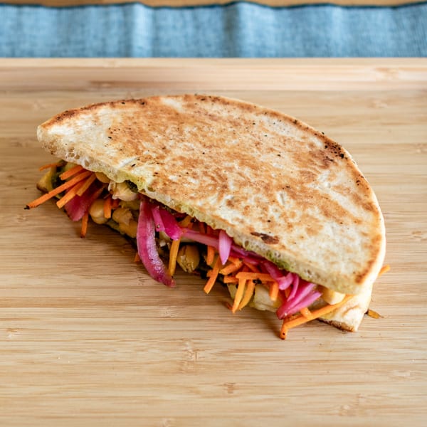 A half-folded Indian flatbread filled with chickpeas, shredded carrots, and pickled red onions on a wooden board.